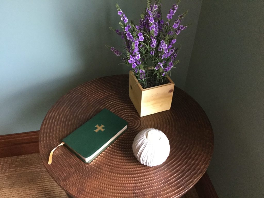 A small table with a bible, flowers and a small ball sitting on it. 